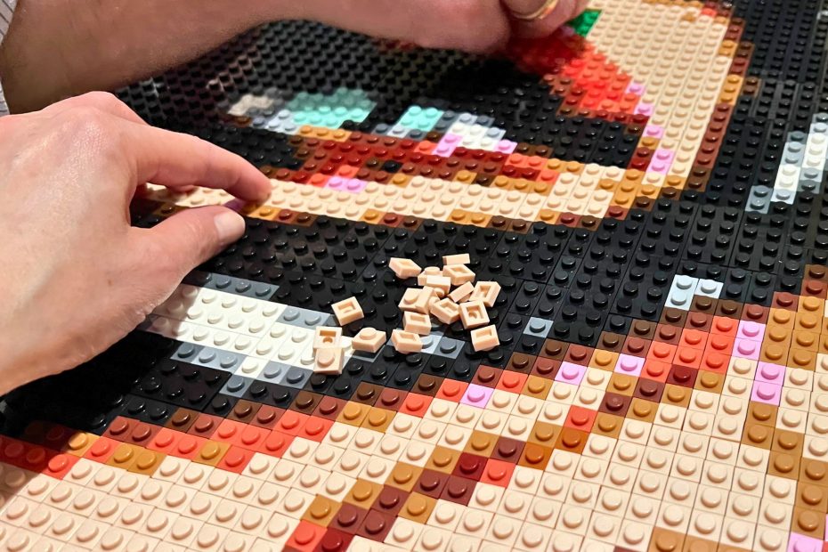 2 persons's hands building a lego compatible brick mosaic of Catwoman