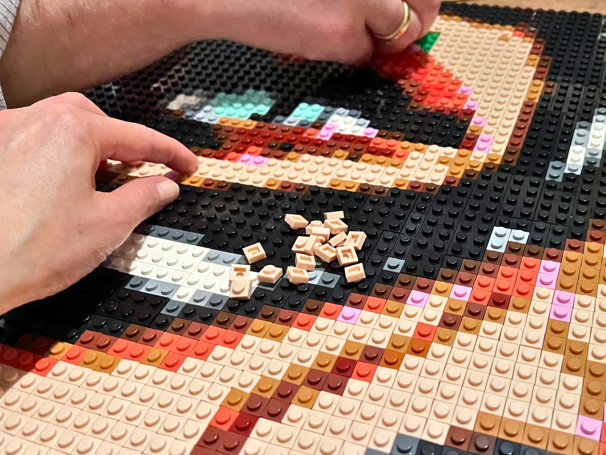 2 persons's hands building a lego compatible brick mosaic of Catwoman